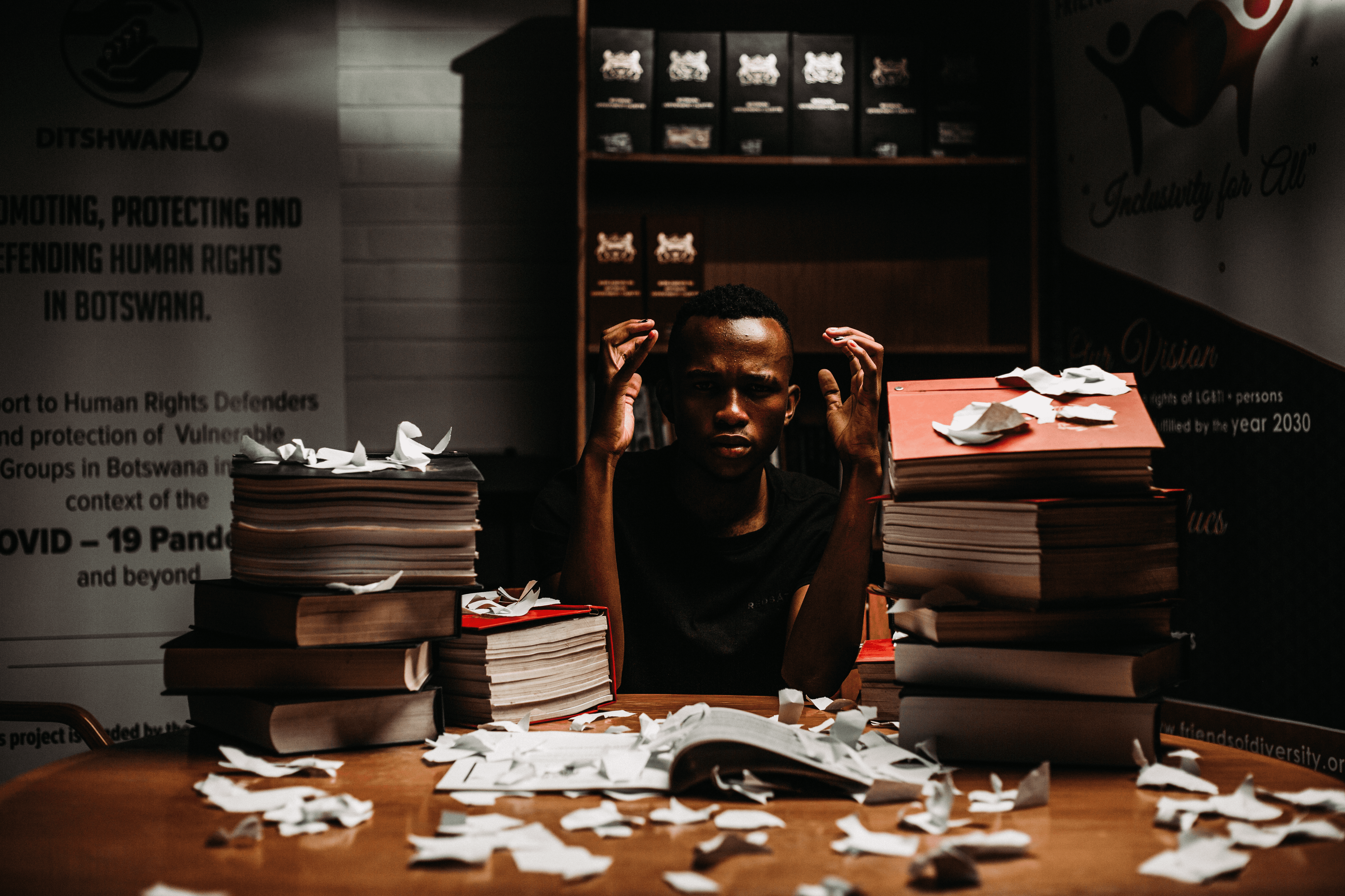 A person sitting on a table piled with files and pieces of torn paper