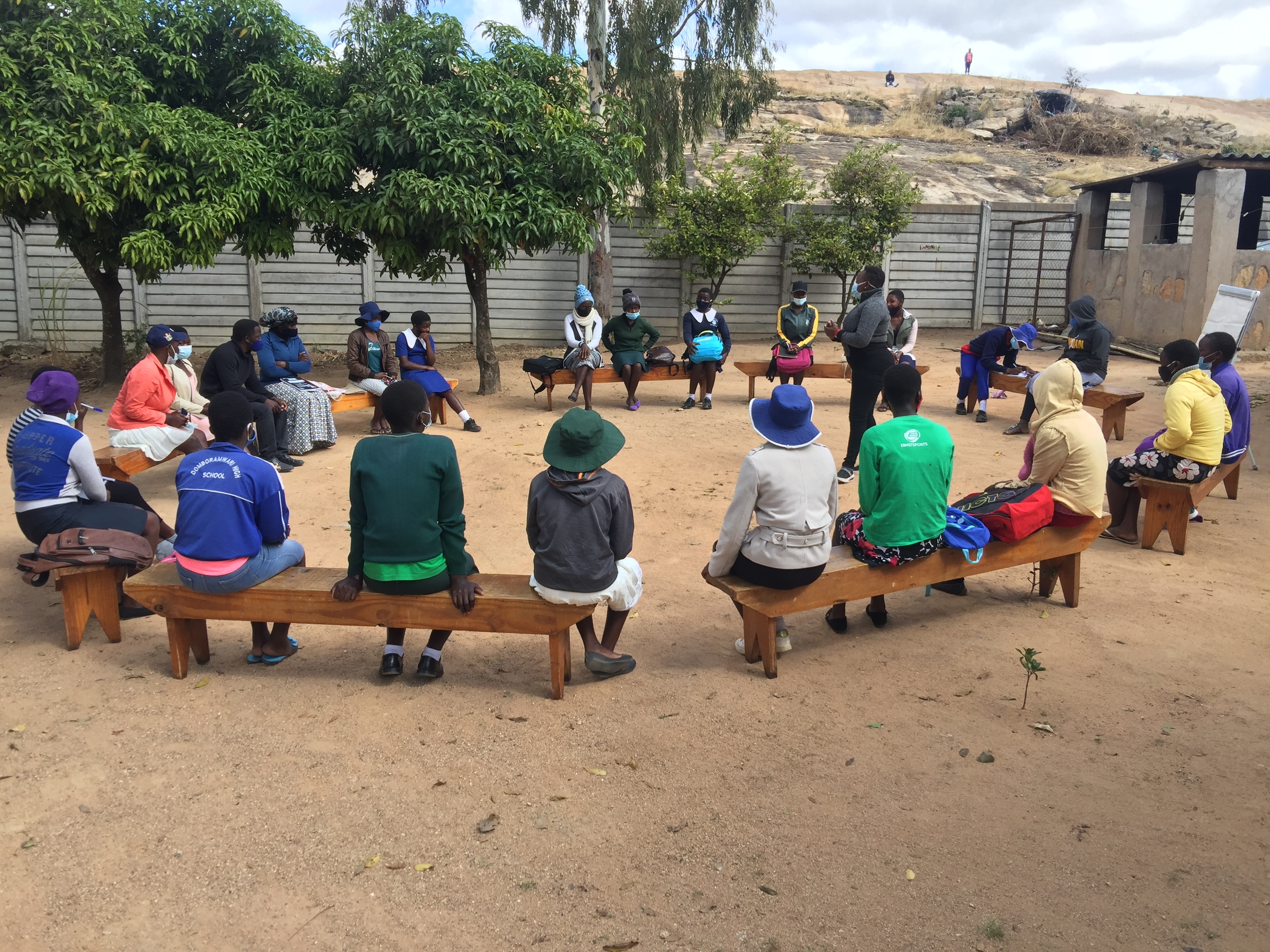 A large group of young women sit in a circle of benches in an outdoor space